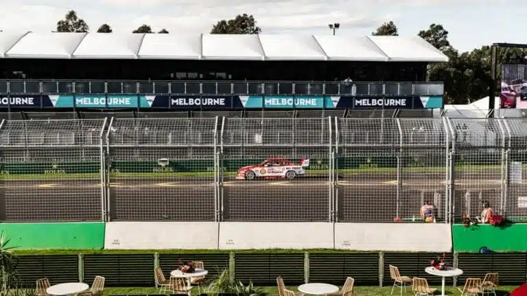 A photograph of a race car driving down a race track featuring banners in the background that say "Melbourne"